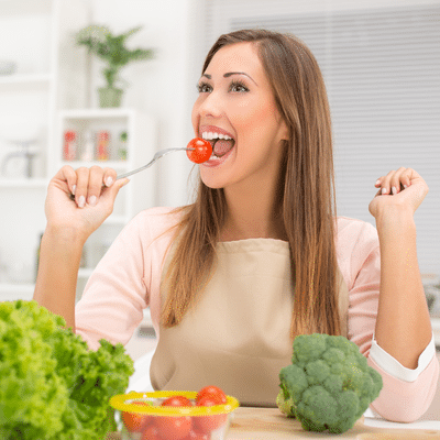 Woman eating vegetables while sitting at a table, representing how diet affects teeth