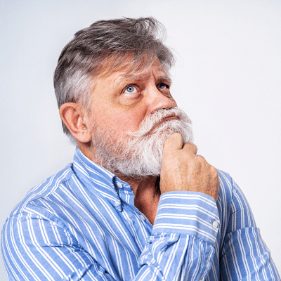 Older man holding his hand to his bearded chin in a state of thinking, representing dentures vs implants