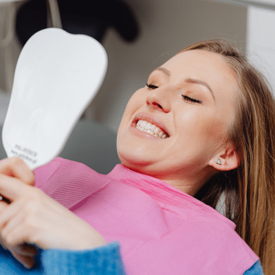 Woman looking at her teeth in a handheld mirror at the dentist, representing causes of tooth discoloration