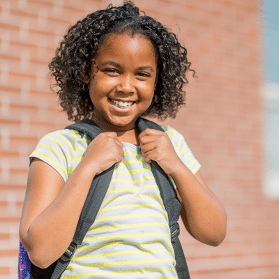 Smiling girl with backpack outdoors, representing tooth friendly foods for kids